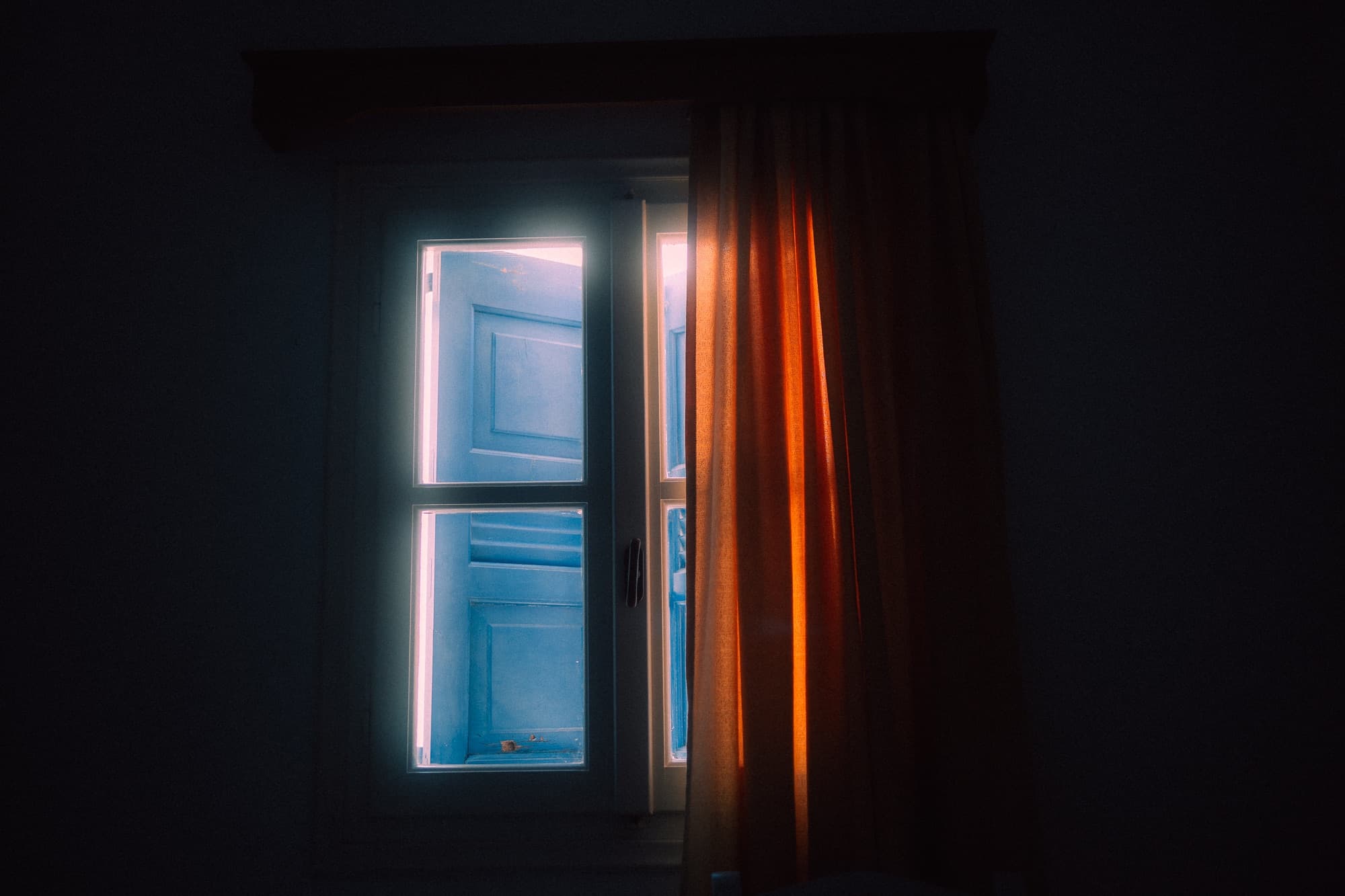 Blue shutters behind a window with an orange curtain