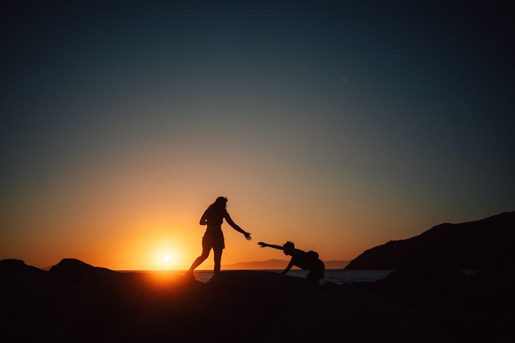 Silhouettes of two people reaching for each other's hands at sunset