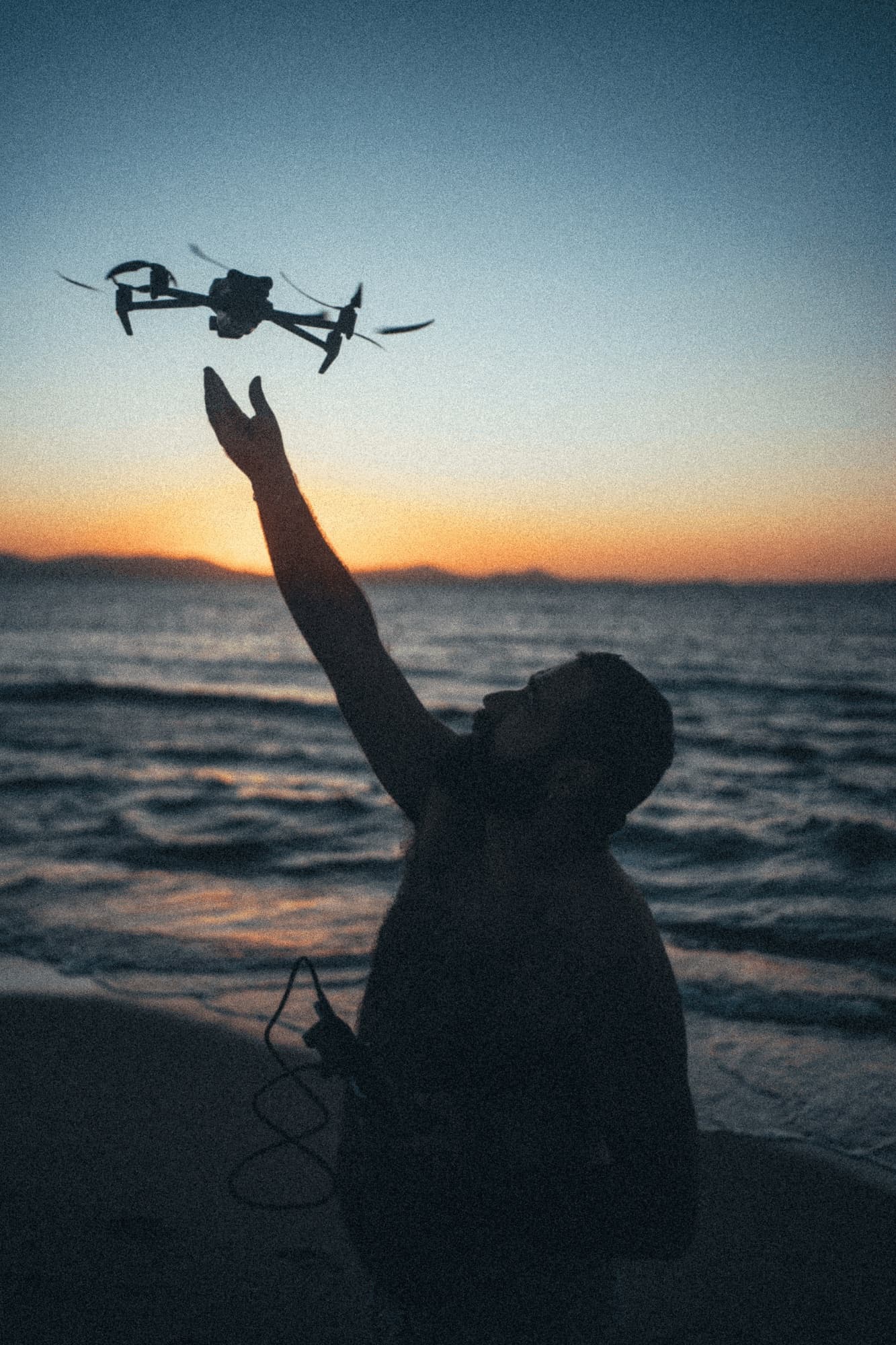 Silhouette of a man catching a drone on a beach at dusk